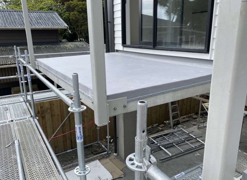 Membrane-lined balcony outside a first-floor window, with scaffolding around it
