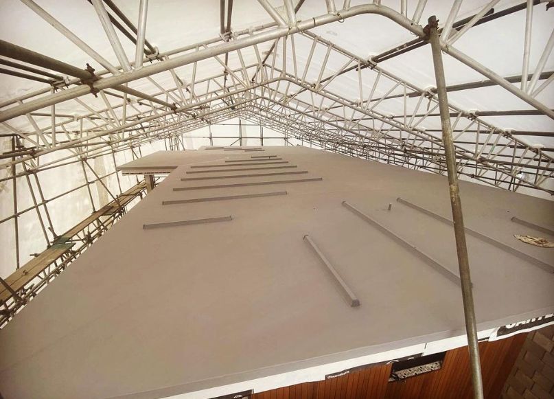 Grey membrane roof with raised batten details, under a scaffold weather enclosure